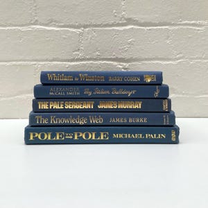 May include: A collection of five navy blue hardback books with gold lettering. Titles visible are "Whitlam to Winston," "My Italian Bulldozer," "The Pale Sergeant," "The Knowledge Web," and "Pole to Pole."