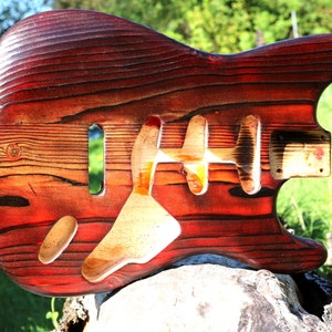 May include: A red and brown wooden guitar body with a natural wood finish. The body is unfinished and has a natural wood grain.