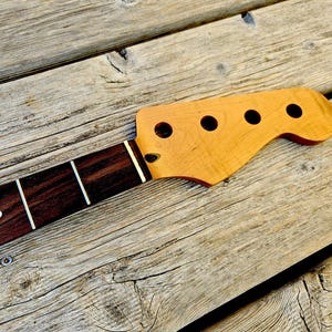 Peut inclure: Un manche de guitare basse doté d'une touche en palissandre brun foncé avec des frettes argentées et une incrustation en point blanc. La tête est fabriquée en bois d'érable clair et comporte quatre trous circulaires pour les mécaniques.