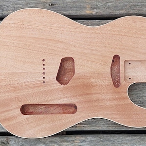 Peut inclure: Un corps de guitare électrique en bois brut de couleur brun clair avec une découpe simple. Le corps présente des cavités pré-découpées pour un chevalet, deux micros et une poche de manche, ainsi que six trous pour les cordes.