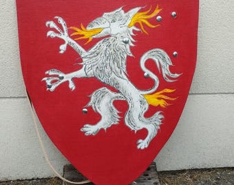 May include: A red shield with a white and silver mythical creature design. The creature has yellow flames emanating from its mouth. The shield has silver rivets and a leather strap.