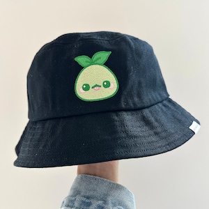 May include: Black bucket hat with a green and light green embroidered cartoon avocado with a pink mouth and pink cheeks.