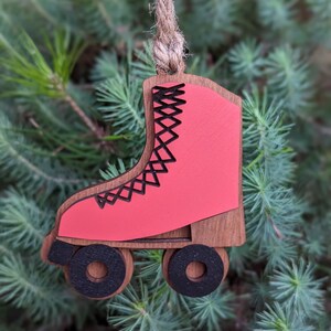 May include: A wooden roller skate ornament with a red painted boot and black wheels. The ornament is hanging from a twine string.