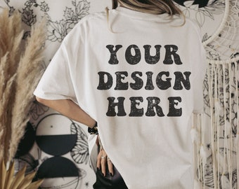 May include: Oversized white t-shirt with the text "YOUR DESIGN HERE" in a distressed black font. The shirt is worn with black leather pants. The model is wearing bracelets and rings.