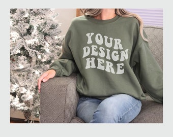 May include: A green sweatshirt with the text "YOUR DESIGN HERE" in white, retro-style lettering. The sweatshirt is being worn by a person sitting on a couch.