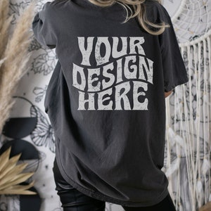 Puede incluir: Una camiseta gris oscuro de gran tama&ntilde;o con el texto "YOUR DESIGN HERE" impreso en blanco en la parte posterior.