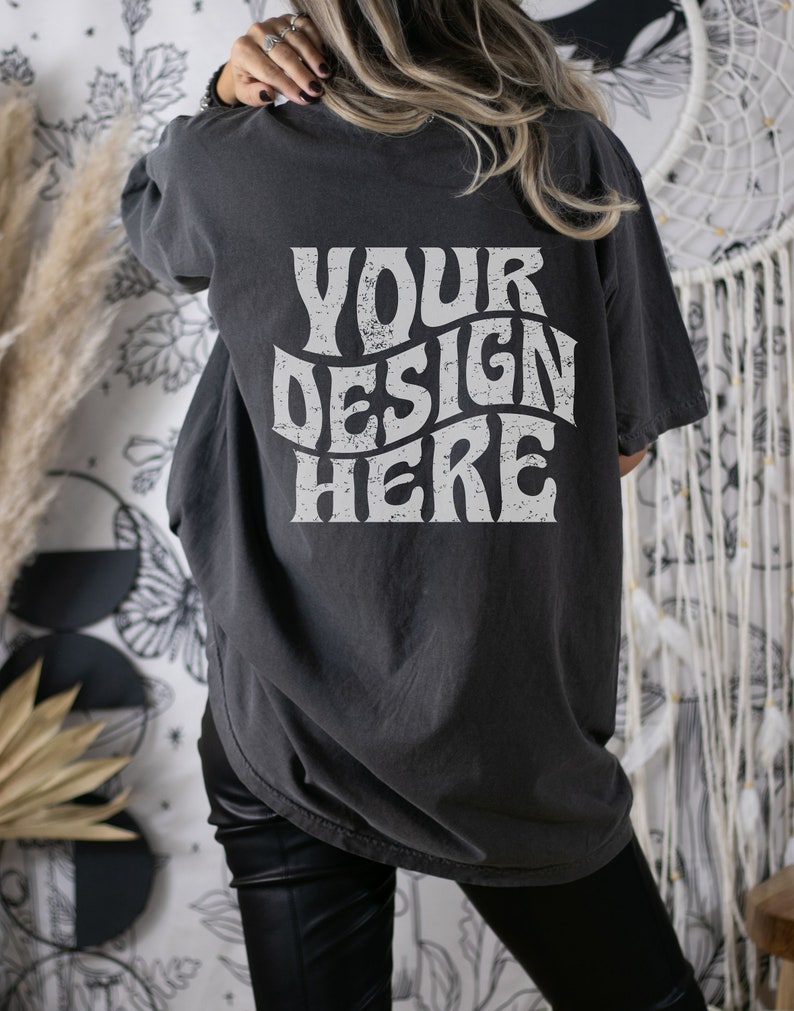 Puede incluir: Una camiseta gris oscuro de gran tama&ntilde;o con el texto "YOUR DESIGN HERE" impreso en blanco en la parte posterior.