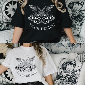 May include: Two t-shirts with a black and white graphic of a moth with wings made of crescent moons. The text "YOUR DESIGN" is printed below the moth on both shirts.