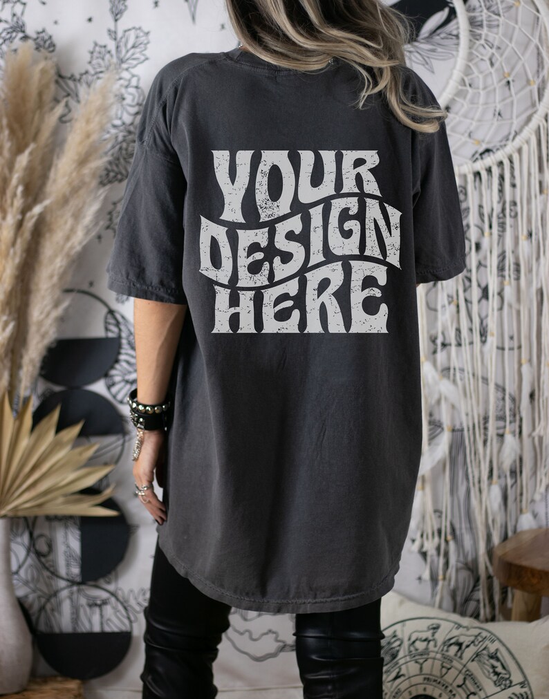 Puede incluir: Una camiseta gris oscuro de gran tama&ntilde;o con el texto "YOUR DESIGN HERE" impreso en blanco en la espalda. El texto est&aacute; en una fuente retro y ondulada.