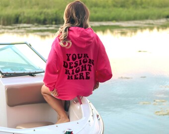 Puede incluir: Una sudadera con capucha rosa con el texto "YOUR DESIGN RIGHT HERE" impreso en la espalda. La sudadera la lleva puesta una persona sentada en un barco blanco.
