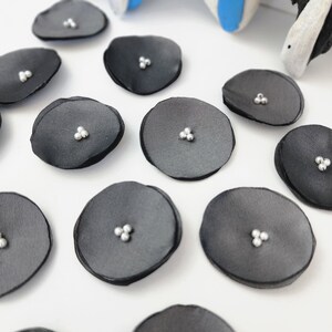 May include: A collection of black fabric circles with three silver beads in the center of each circle.