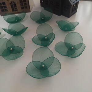 Könnte beinhalten: Dunkelgrüne, transparente Stoffblumenverzierungen mit einem Perlenmittelpunkt. Die handgefertigten floralen Akzente sind auf einer weißen Oberfläche angeordnet. Dekorative Elemente für Bastelarbeiten, Nähen oder andere DIY-Projekte.