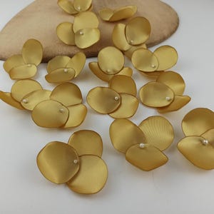 Könnte beinhalten: Eine Sammlung von 15 goldenen Satin-Blütenblättern mit einer Perle in der Mitte jedes Blütenblattes.