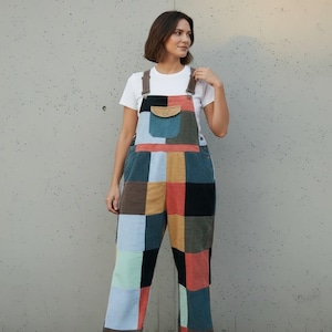 May include: Corduroy overalls featuring a patchwork design with various rectangular panels in shades of blue, brown, orange, black, and tan. The garment includes a front bib pocket with a button closure, adjustable shoulder straps, and side buttons.