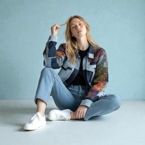 Op de afbeelding: Een spijkerjasje met patchwork mouwen en een lichtblauwe wassing, gecombineerd met lichtblauwe jeans en witte sneakers. De jas heeft een mix van denim en stof met patronen.