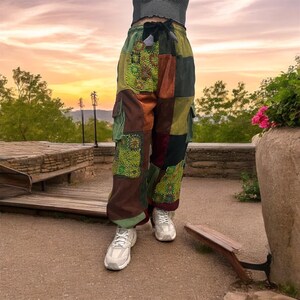 Puede incluir: Pantal&oacute;n cargo de patchwork con cintura de cord&oacute;n y varios bolsillos. El pantal&oacute;n est&aacute; hecho de una variedad de telas en tonos de marr&oacute;n, verde y rojo. El pantal&oacute;n lo lleva puesto una persona que est&aacute; de pie en un camino de piedra.
