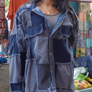 May include: A patchwork denim jacket in shades of blue. The jacket has a button-up front, pockets, and a frayed hem. The garment is made of different denim squares sewn together, creating a unique, textured appearance. The jacket is a stylish piece of clothing.