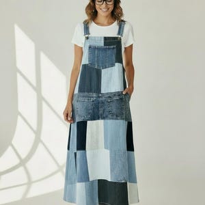 May include: A floor-length denim overall dress featuring a patchwork design with various shades of blue, ranging from light to dark indigo. The dress includes a front chest pocket, two side pockets, and adjustable shoulder straps with metal buckles.