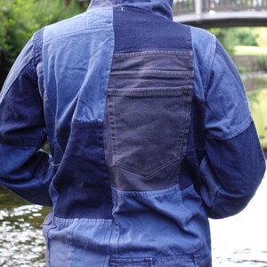 May include: A patchwork denim jacket with a hood, featuring various shades of blue. The back of the jacket has a large pocket and a textured hem. The jacket is designed with a mix of denim panels.