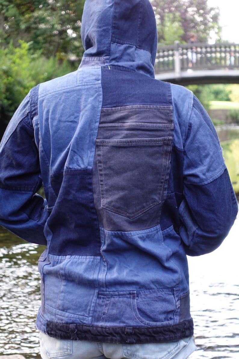 May include: A patchwork denim jacket with a hood, featuring various shades of blue. The back of the jacket has a large pocket and a textured hem. The jacket is designed with a mix of denim panels.