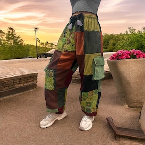 Op de afbeelding: Patchwork broek met een trekkoord in de taille en grote cargozakken. De broek is gemaakt van verschillende stoffen in tinten groen, bruin en rood.