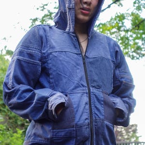 May include: A blue hooded jacket with a full-length zipper and front pockets. The jacket has a patchwork design with varying shades of blue denim. The hood is up, and the jacket appears to be worn outdoors.