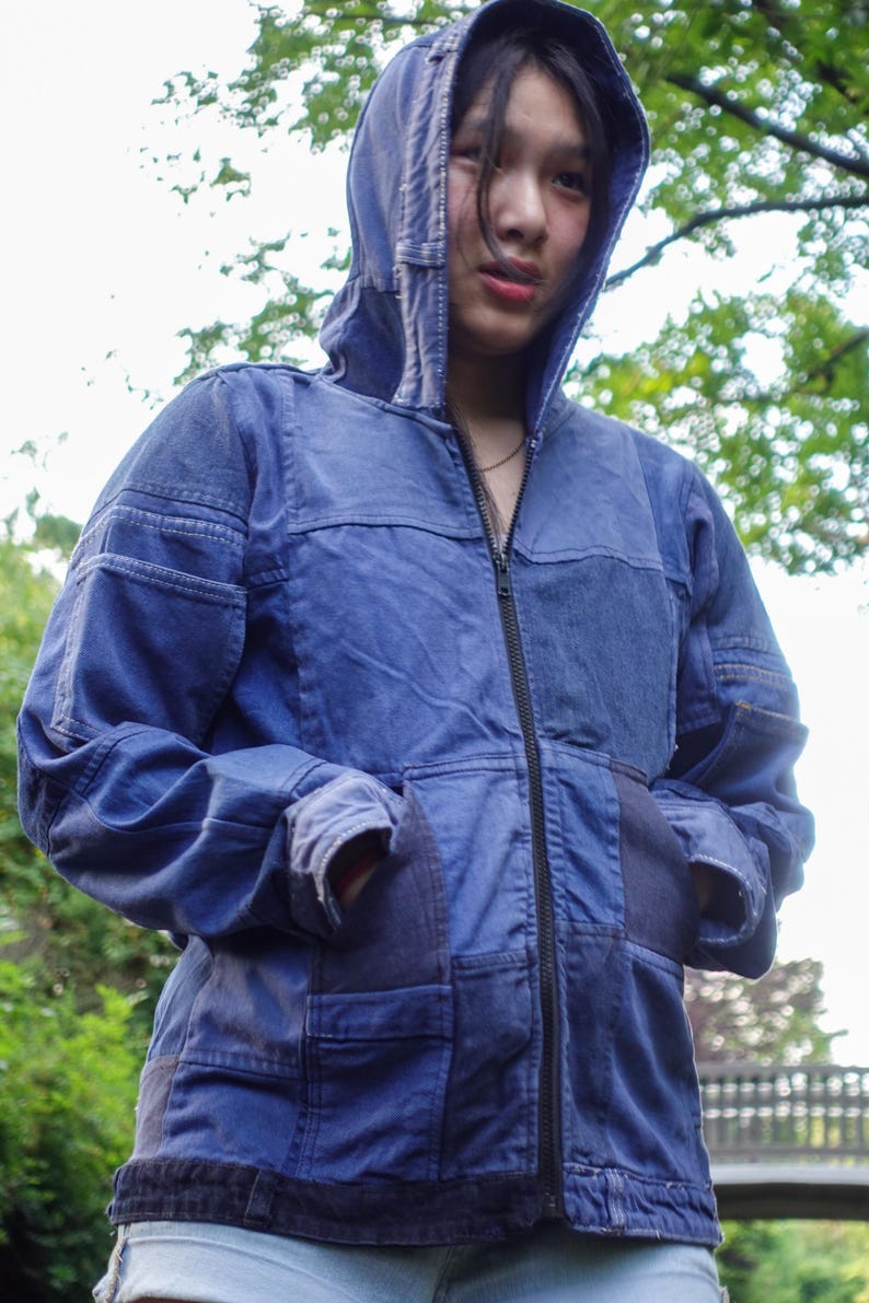 May include: A blue hooded jacket with a full-length zipper and front pockets. The jacket has a patchwork design with varying shades of blue denim. The hood is up, and the jacket appears to be worn outdoors.