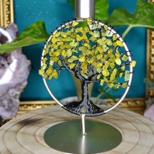 Könnte beinhalten: Ein silberner Baum des Lebens Kerzenhalter aus Metall mit einem Design aus gelben Edelsteinen. Der Halter steht auf einem Holzsockel.