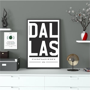 Könnte beinhalten: Ein gerahmter Schwarz-Weiß-Druck mit dem Wort "DALLAS" in fetten Großbuchstaben. Darunter stehen die Koordinaten 32° 46' 45.60" N und 96° 48' 32.40" W und der Text "U.S.A."