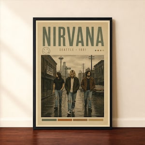 Pode incluir: Um cartaz emoldurado da banda Nirvana com o texto NIRVANA SEATTLE 1991. A imagem mostra três pessoas caminhando por uma rua da cidade com uma torre alta ao fundo e uma placa SUB POP em um prédio de tijolos à esquerda.