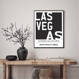 Könnte beinhalten: Ein gerahmter Schwarz-Weiß-Druck mit dem Text "LAS VEGAS" in einer kräftigen, modernen Schriftart. Darunter befinden sich die Koordinaten. Der Text "UNITED STATES OF AMERICA" befindet sich am unteren Rand.