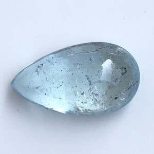Puede incluir: Una piedra preciosa de aguamarina en forma de lágrima, de color azul claro y con una superficie lisa y pulida.