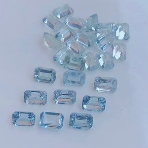 Puede incluir: Una colección de gemas de color azul claro, talladas en forma rectangular. Las gemas están dispersas sobre una superficie blanca, con diferentes tamaños y facetas. La apariencia general es clara y brillante.