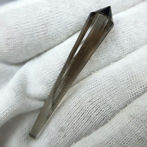 May include: A dark gray faceted crystal point with a pointed tip.