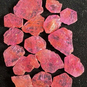 May include: A collection of pink ruby crystals, some with a translucent appearance, on a black background.