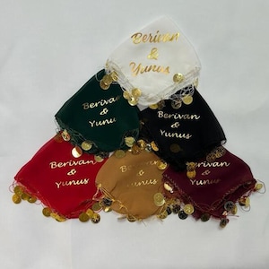 Könnte beinhalten: Eine Sammlung farbiger Taschentücher, jedes mit goldenem Text "Berivan & Yunus". Die Taschentücher sind in verschiedenen Farben erhältlich: Weiß, Grün, Schwarz, Rot, Braun und Burgunder. Jedes Taschentuch ist mit goldfarbenen Münzverzierungen versehen.