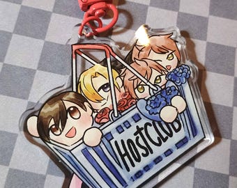 May include: Clear acrylic keychain featuring an anime-style illustration of four characters in a shopping cart. The cart is labeled "HOST CLUB" in blue and white. The keychain has a red clasp.