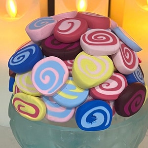 May include: A colorful assortment of handmade polymer clay swirl designs in various shades of blue, pink, yellow, and brown. The swirls are arranged in a circular pattern, creating a visually appealing and unique design.