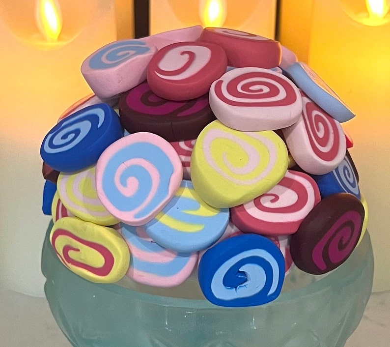 May include: A colorful assortment of handmade polymer clay swirl designs in various shades of blue, pink, yellow, and brown. The swirls are arranged in a circular pattern, creating a visually appealing and unique design.