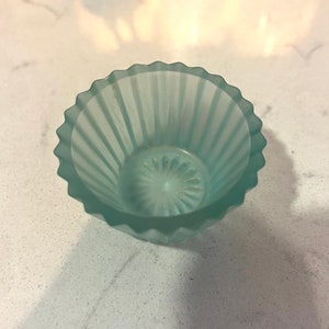 May include: A small, light blue glass bowl with a fluted design. The bowl is frosted and has a slightly iridescent finish.