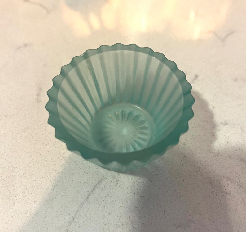 May include: A small, light blue glass bowl with a fluted design. The bowl is frosted and has a slightly iridescent finish.