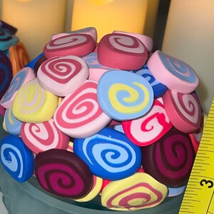 May include: A blue ceramic bowl filled with colorful swirl-shaped clay decorations. The decorations are in shades of pink, yellow, blue, purple, and red.