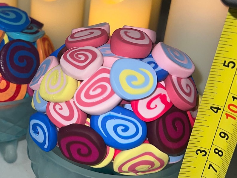 May include: A blue ceramic bowl filled with colorful swirl-shaped clay decorations. The decorations are in shades of pink, yellow, blue, purple, and red.