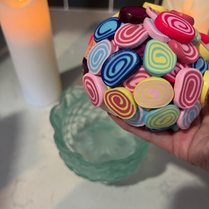 May include: A colourful ball made of small, rolled clay pieces. The pieces are in shades of pink, yellow, blue, and red, with white and yellow swirls.