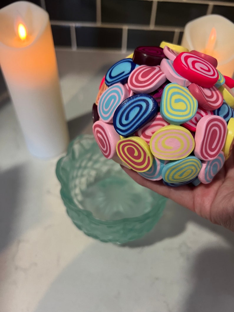 May include: A colourful ball made of small, rolled clay pieces. The pieces are in shades of pink, yellow, blue, and red, with white and yellow swirls.