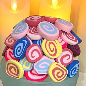 May include: A pile of colorful, swirled clay pieces in various shades of pink, blue, yellow, and red. The clay pieces are arranged in a mound, creating a visually appealing and textured display.