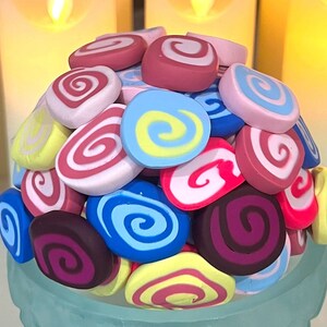 May include: A collection of colorful swirl-patterned candy, arranged in a pile. The candy is in shades of pink, blue, red, yellow, and purple.