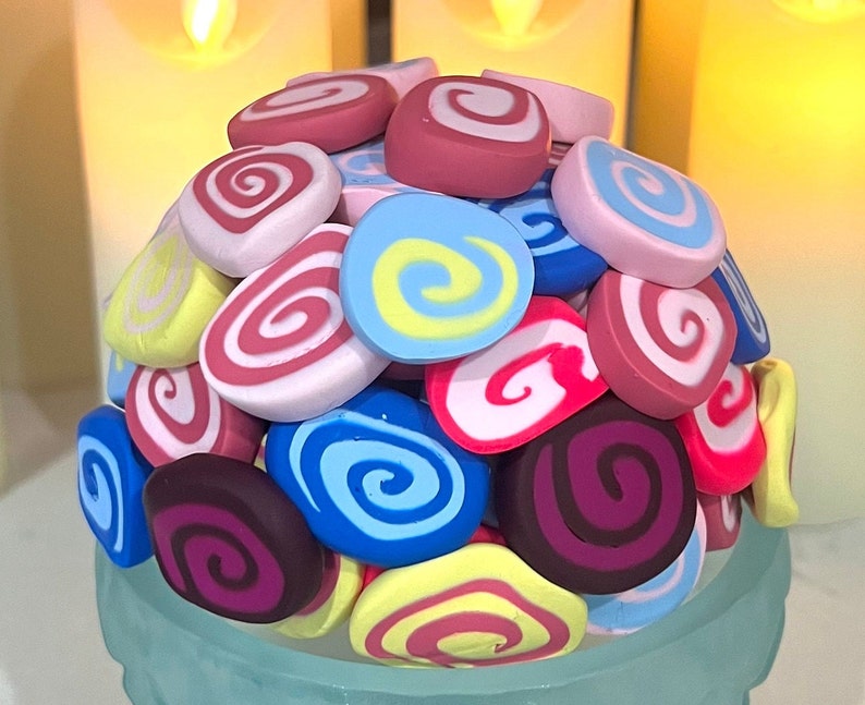 May include: A collection of colorful swirl-patterned candy, arranged in a pile. The candy is in shades of pink, blue, red, yellow, and purple.