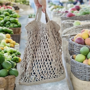 Puede incluir: Un bolso de cuerda de crochet marrón con un asa anudada. El bolso está hecho de fibra natural y tiene un tejido suelto.