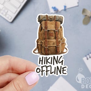 May include: A die-cut sticker featuring a brown canvas backpack with leather straps and a rolled sleeping bag on top. Below the backpack, the text HIKING OFFLINE is printed in bold, black, sans-serif capital letters against a white background.